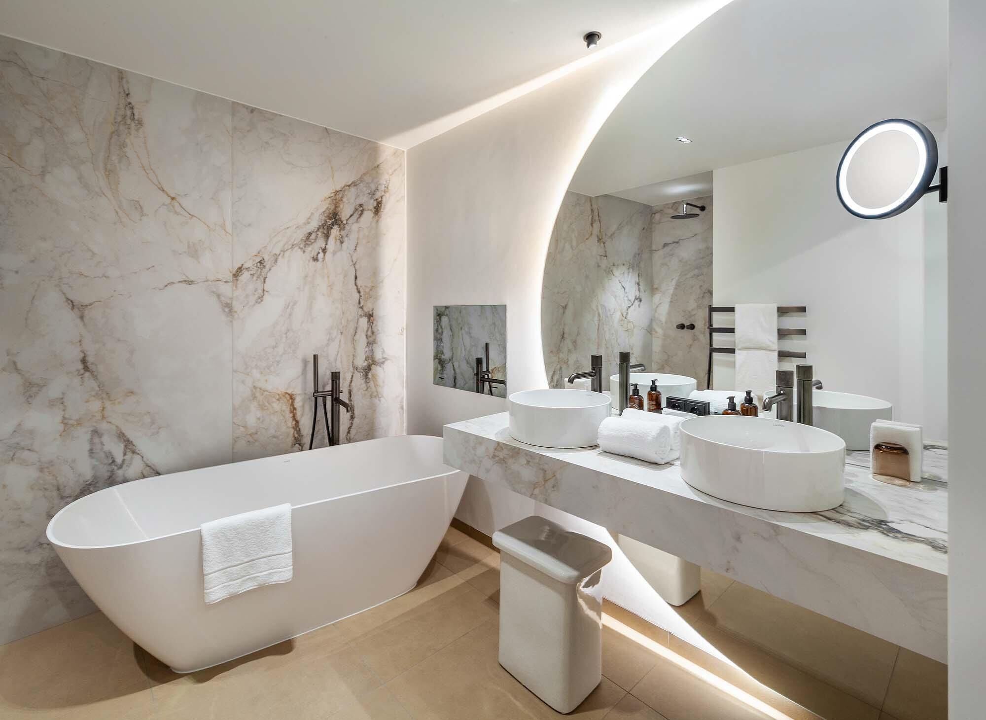 A modern bathroom with a freestanding bathtub, two sinks, and a large mirror.