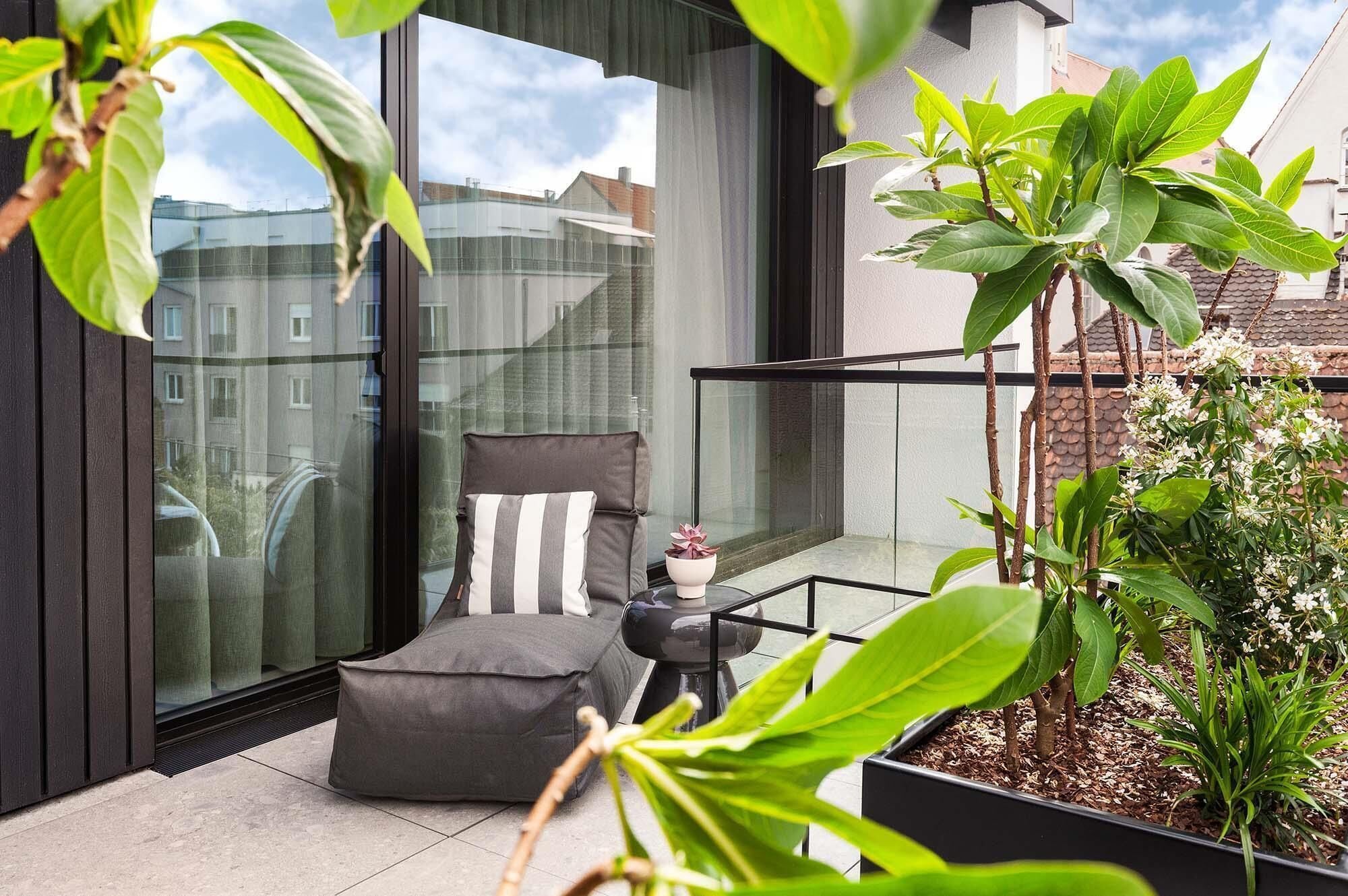 A balcony with a glass door, a cushioned seating area, and a potted plant.