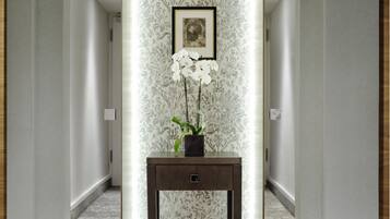 Un couloir avec un papier peint à motifs, un tableau encadré posé sur une console et une orchidée en pot.