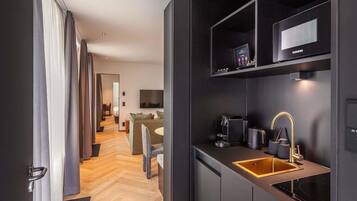 Quarto de hotel moderno com cozinha compacta, televisão de tela plana e área de refeições com mesa e cadeiras.