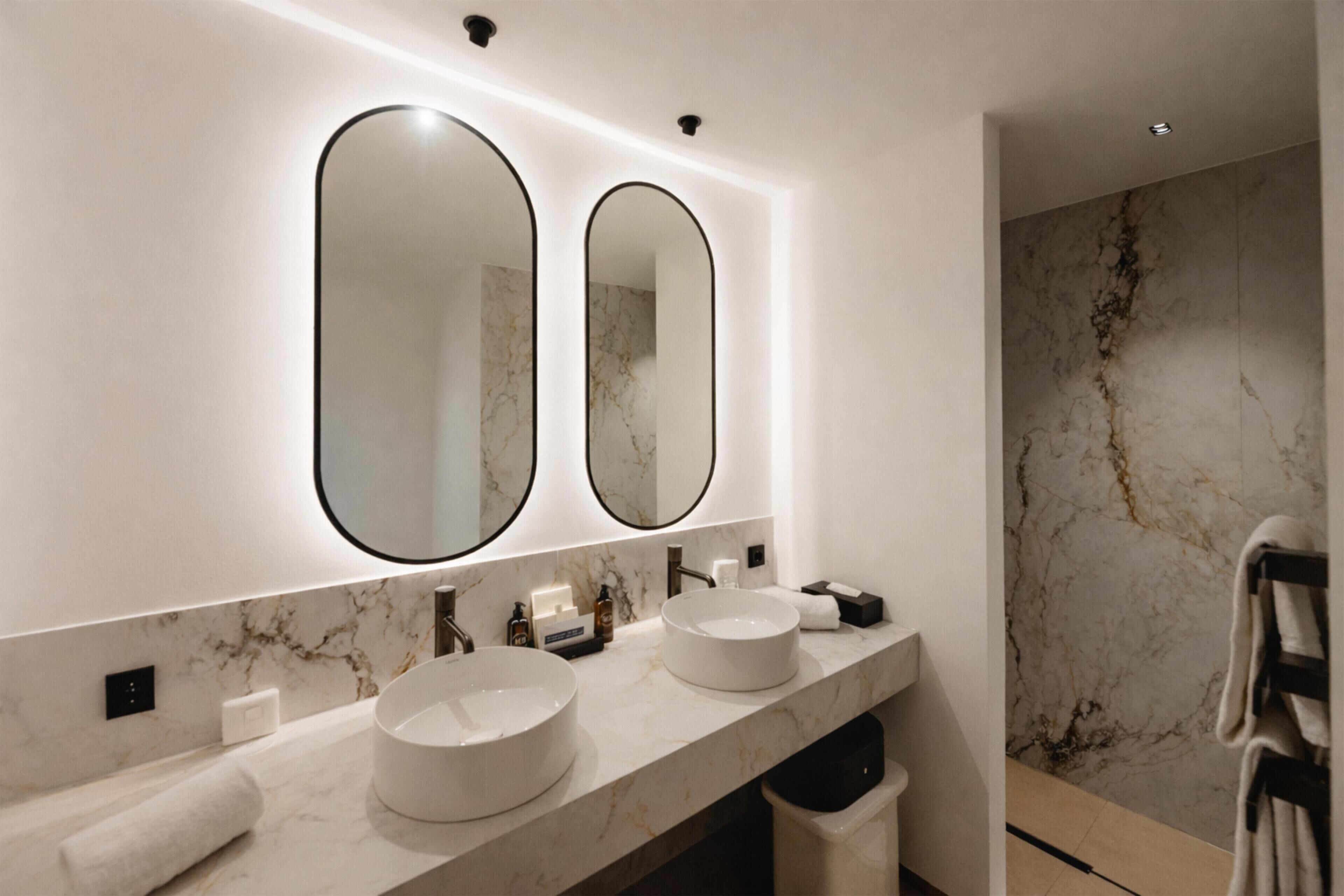 A bathroom with two sinks, a large mirror, and a marble wall.