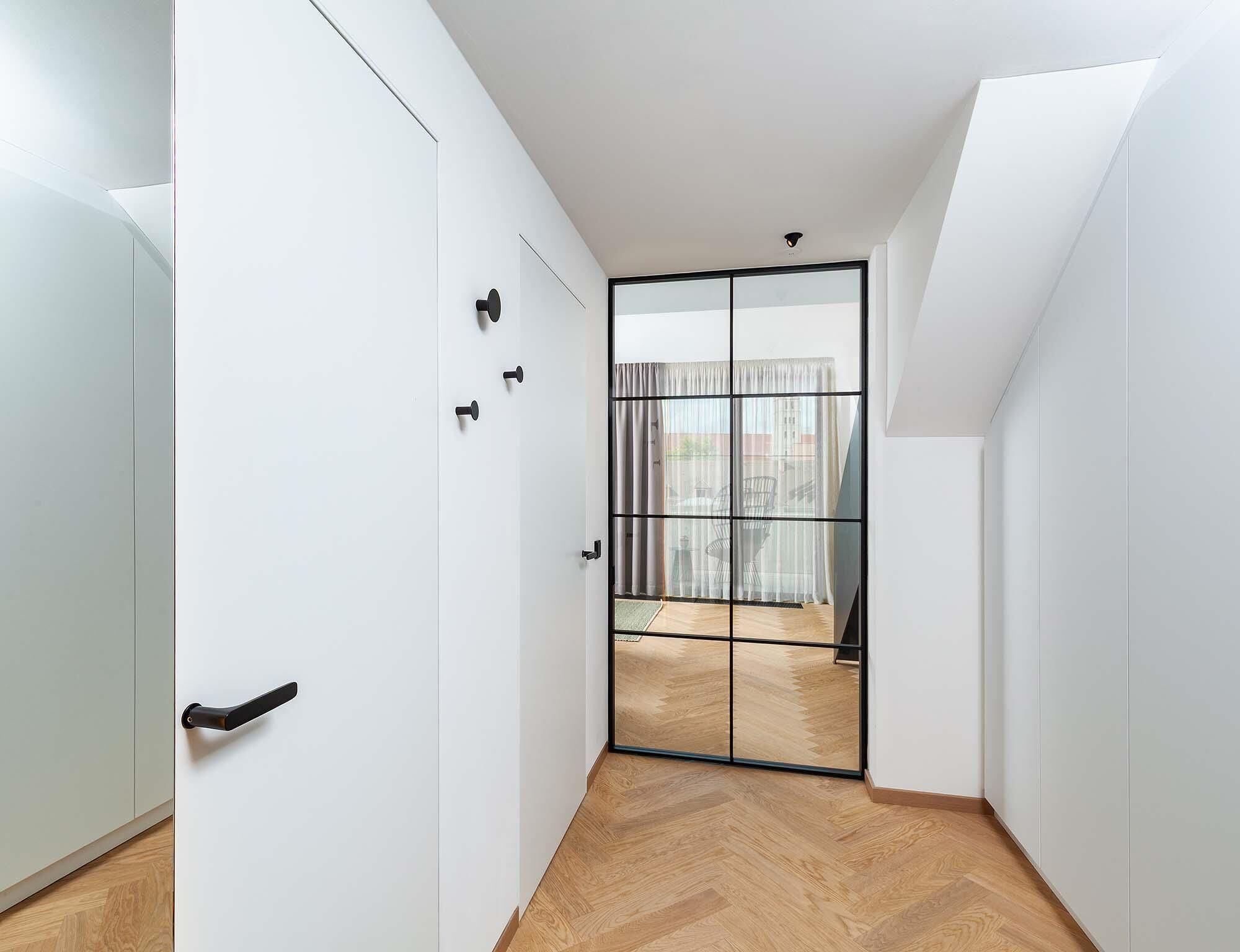 Un pasillo con piso de madera, paredes blancas y un ventanal corredero que da a un espacio exterior con vistas.