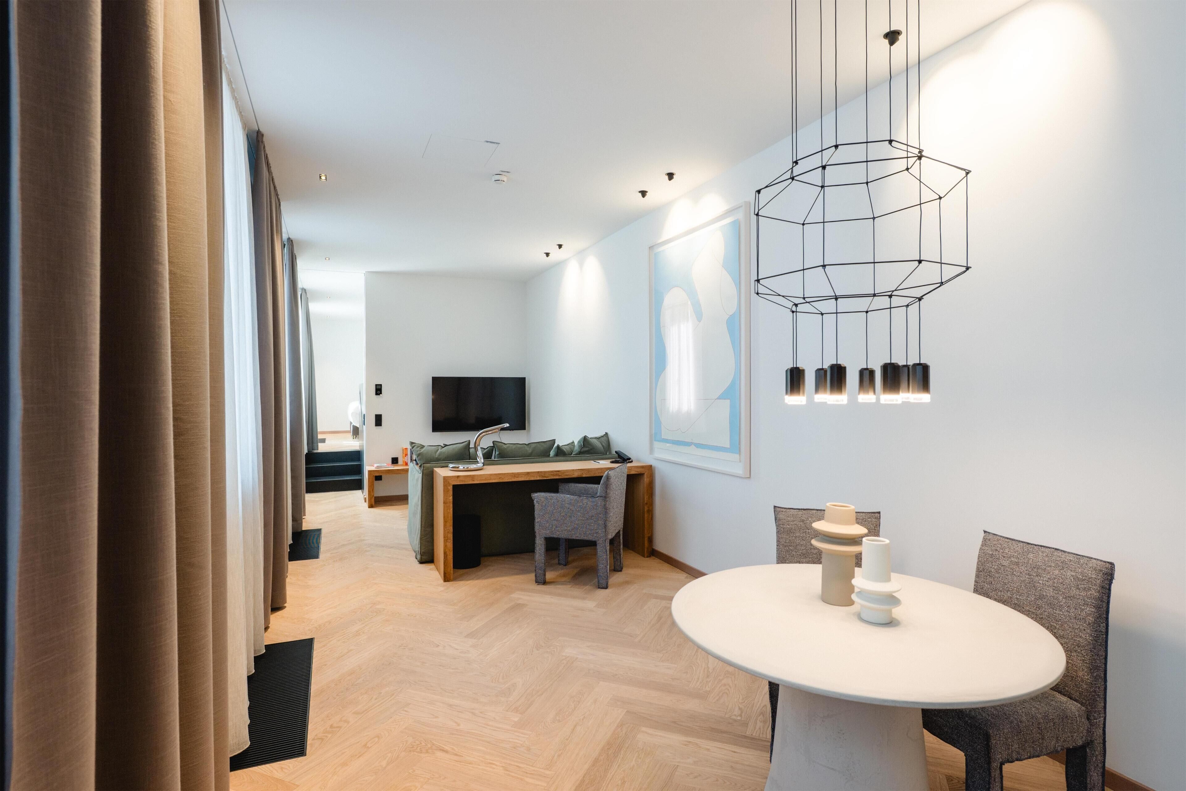 Een moderne hotelkamer met een houten bureau, een televisie, een eettafel en een bijzondere geometrische lamp.