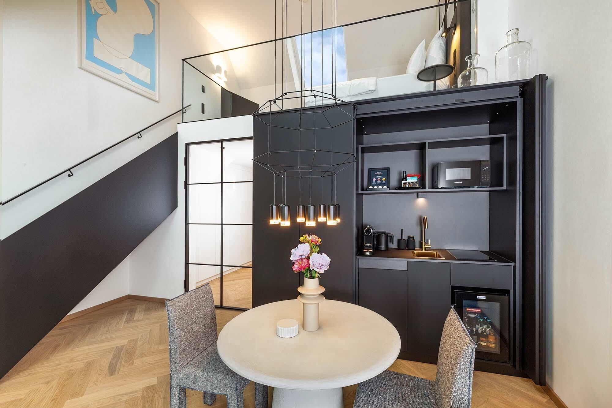 A modern interior with a staircase, a dining area with a round table, and a kitchen area with appliances.