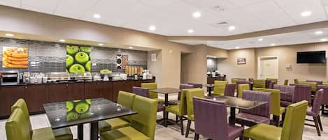 A restaurant with green and purple chairs, a buffet counter, and a television on the wall.