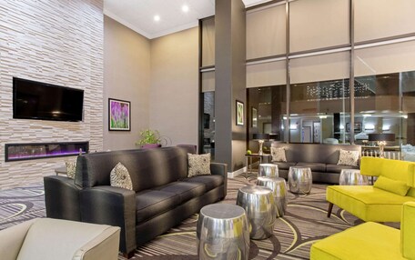 A modern hotel lobby with a black leather sofa, yellow armchair, and metallic side tables.