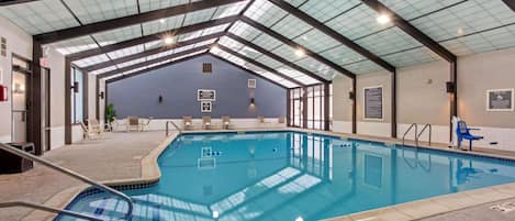An indoor swimming pool with clear blue water, surrounded by lounge chairs and a covered roof structure.