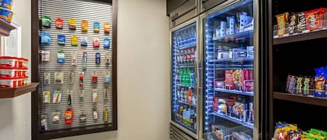 Un área de venta automática con opciones de bocadillos y bebidas, que incluye una sección refrigerada para bebidas y un expositor mural de aperitivos.