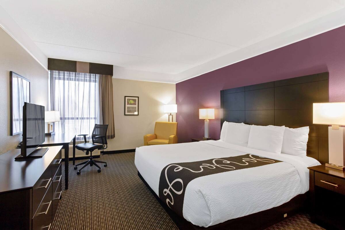 Una camera d'albergo con un letto grande, una scrivania con una sedia, una televisione e due lampade.