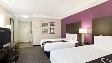 A hotel room with two beds, a television, a desk, and a lamp.