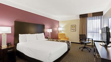 A hotel room with a large bed, a desk with a computer, a chair, and a TV.