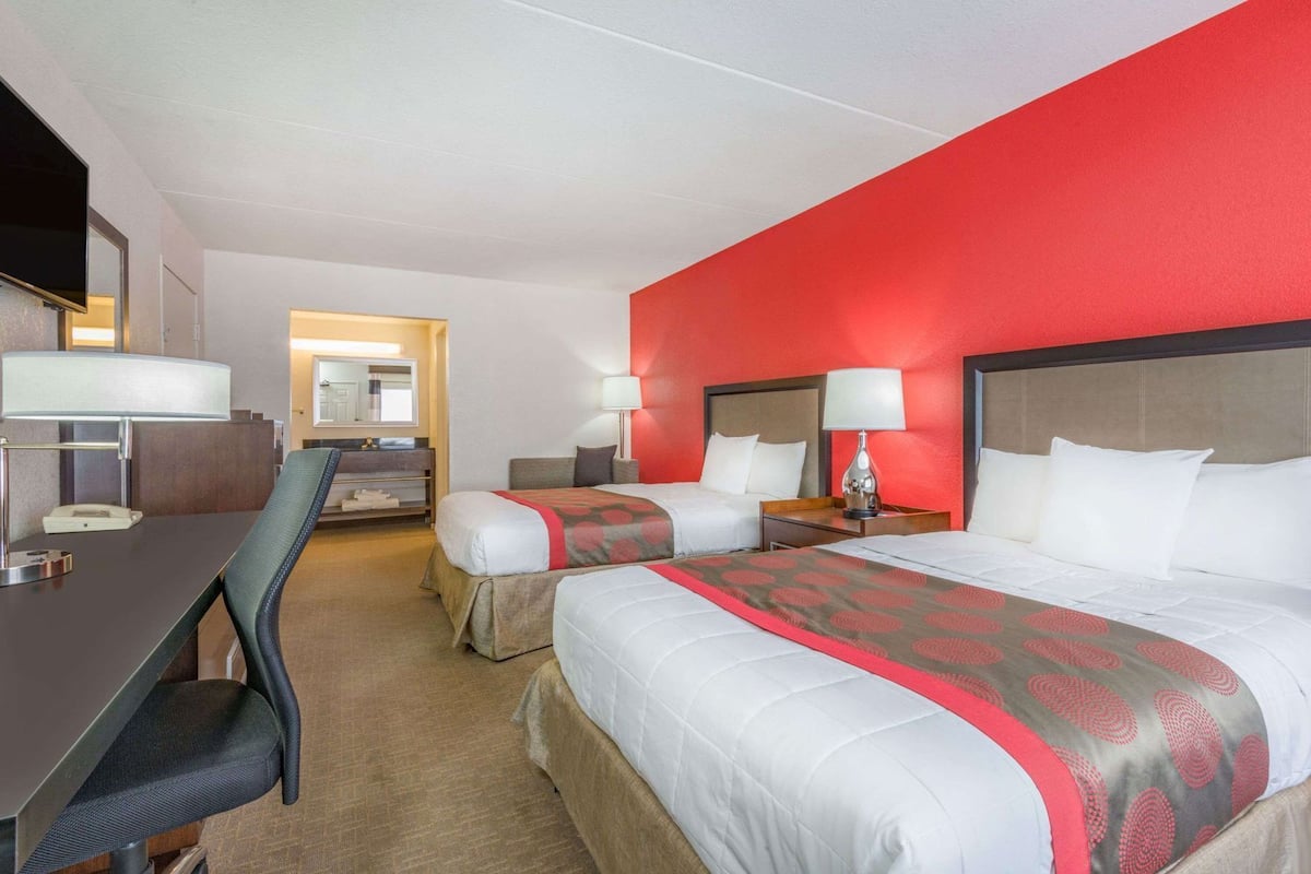 A hotel room with two beds, a desk, a chair, and a TV.