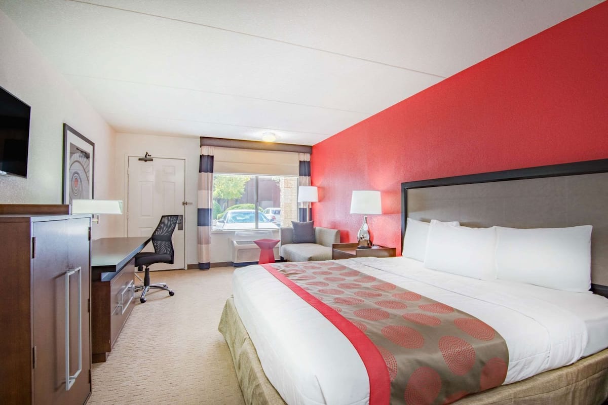 A hotel room with a bed, desk, chair, and a view of the outside.