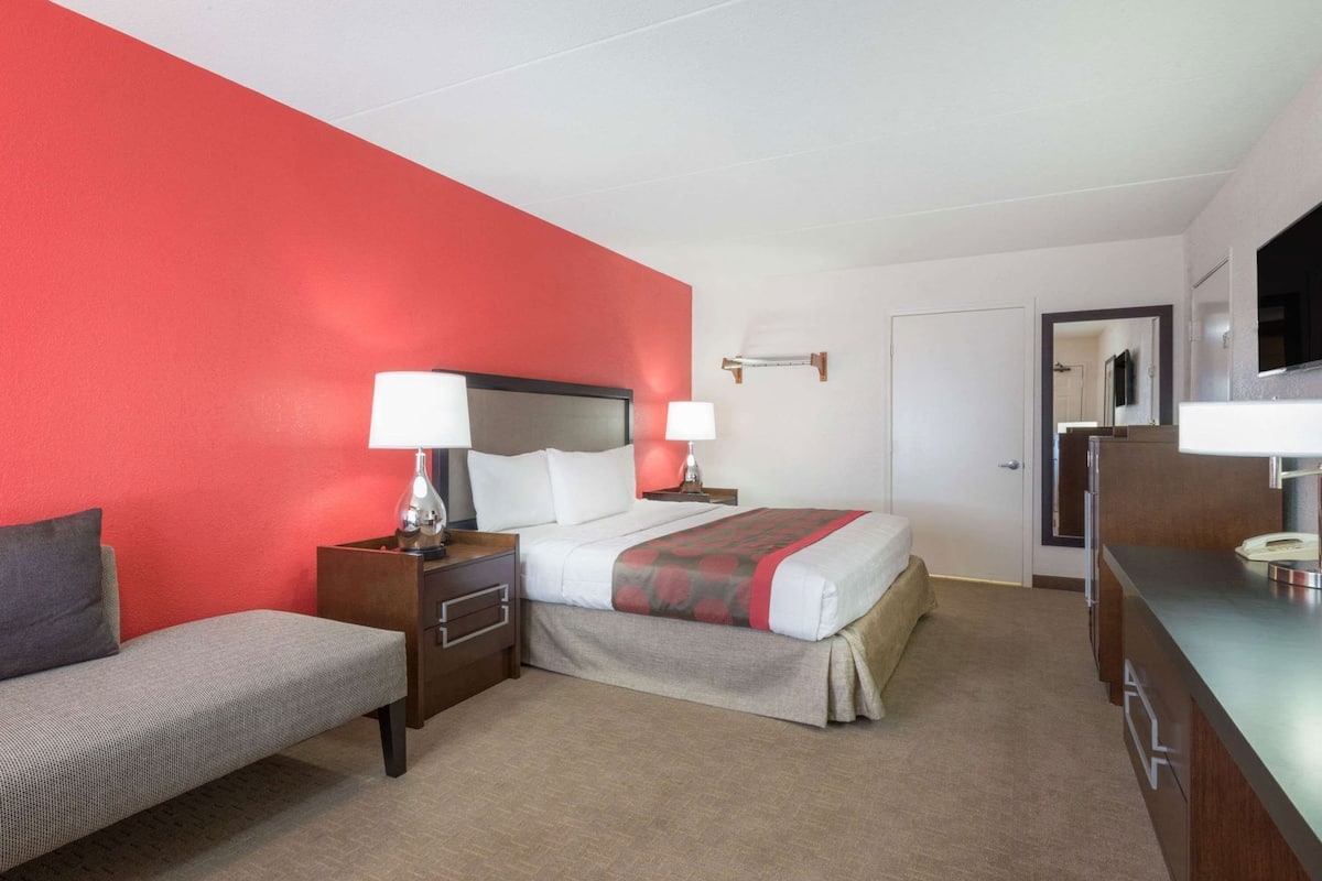 A hotel room with a bed, bedside tables, a chair, a desk, and a TV.