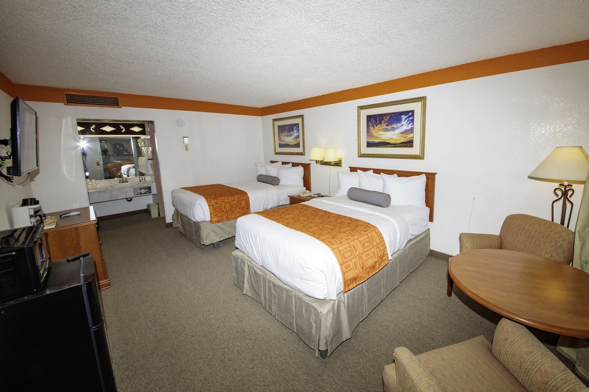 A hotel room with two beds, a desk, a chair, and a dining table.