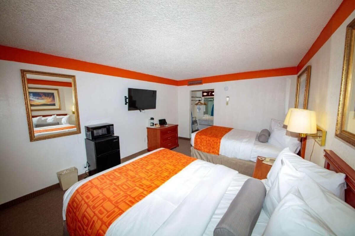 A hotel room with two beds, a television, a desk, and a mirror.
