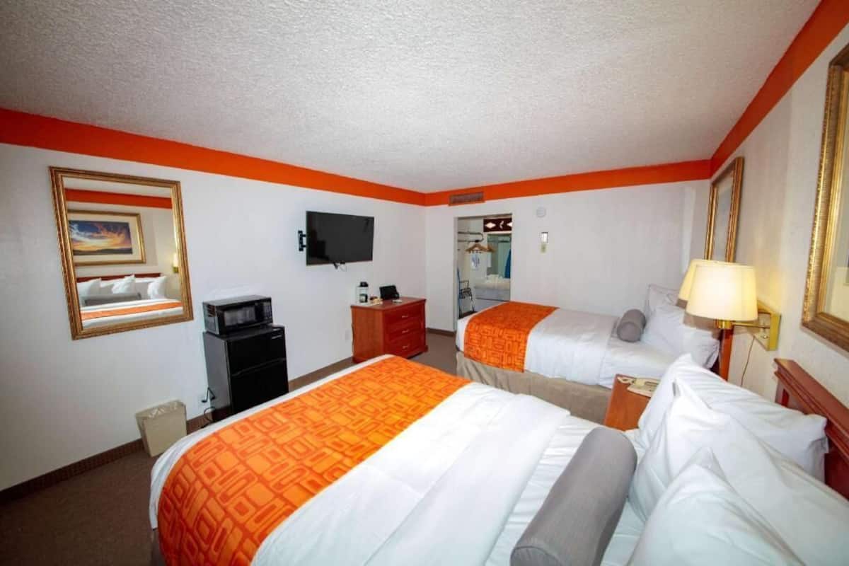 A hotel room with two beds, a television, a desk, and a mirror.