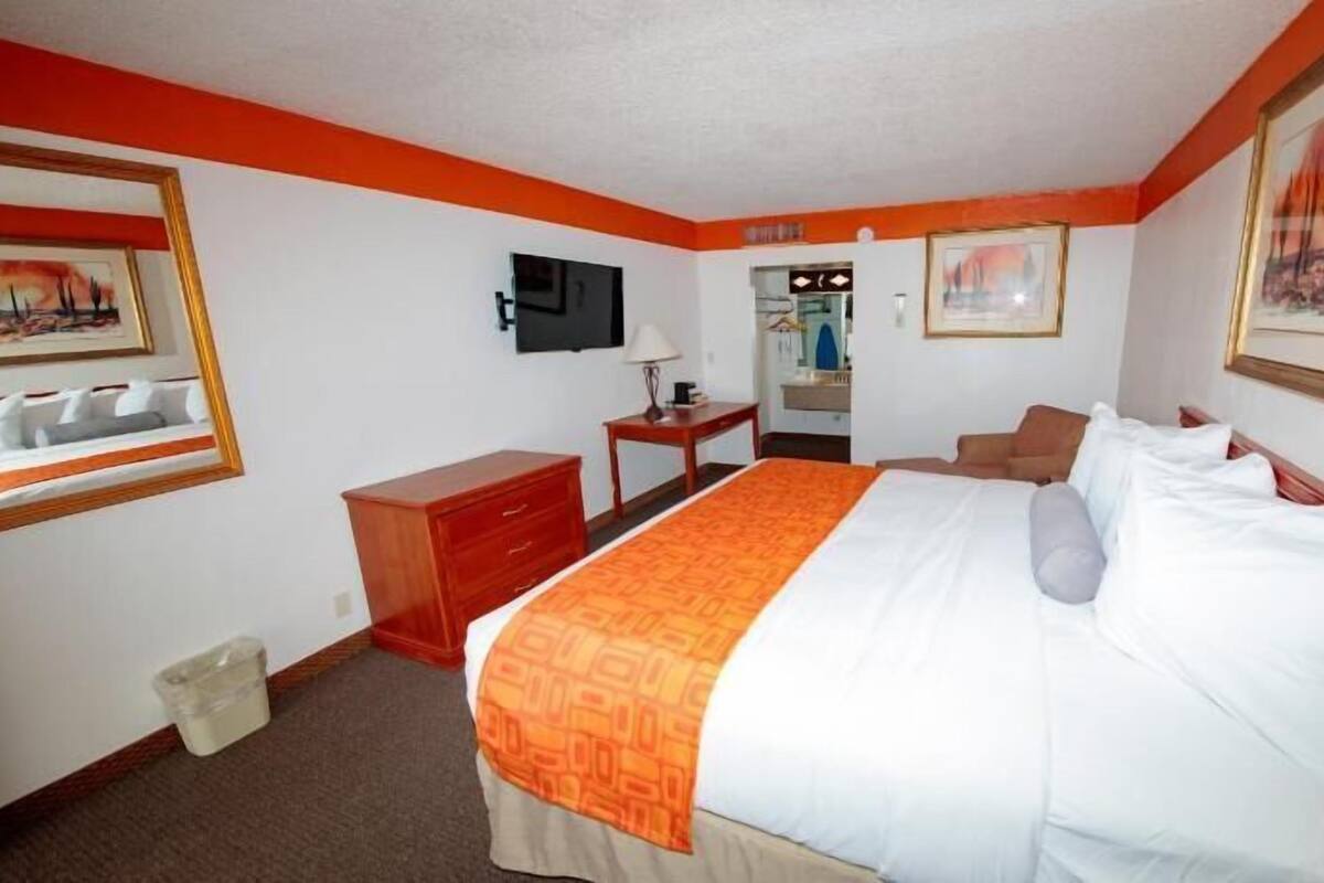 A hotel room with a bed, a desk, a chair, a television, and a bathroom visible through an open door.
