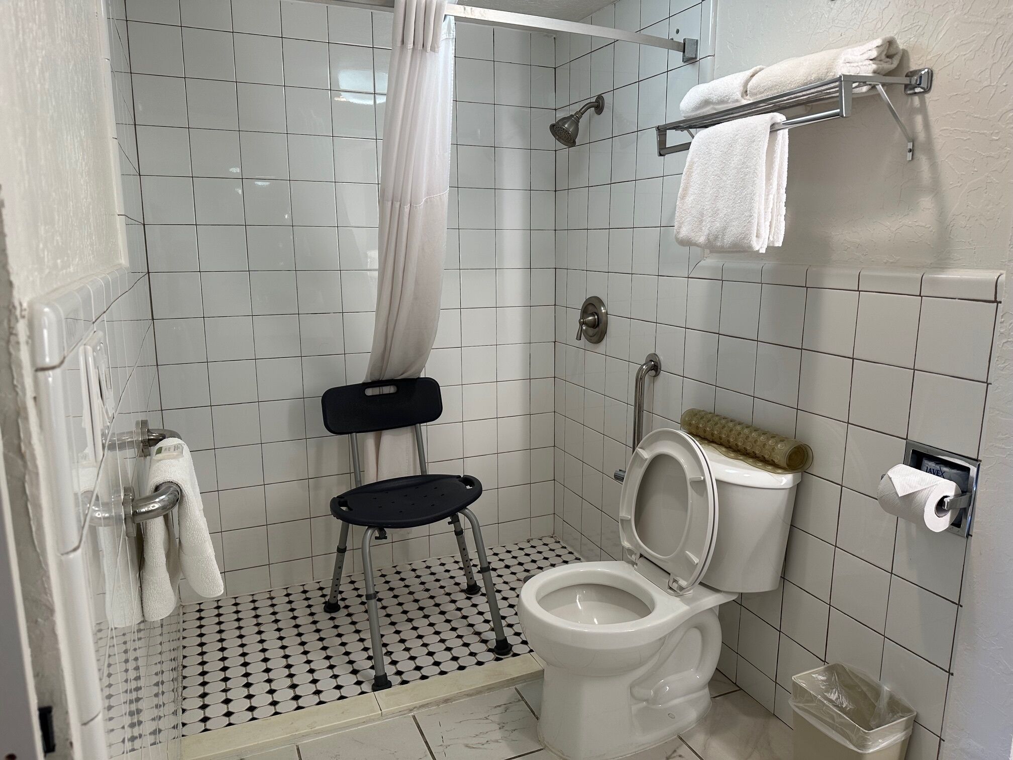 Un baño con ducha, inodoro y una pequeña silla negra.