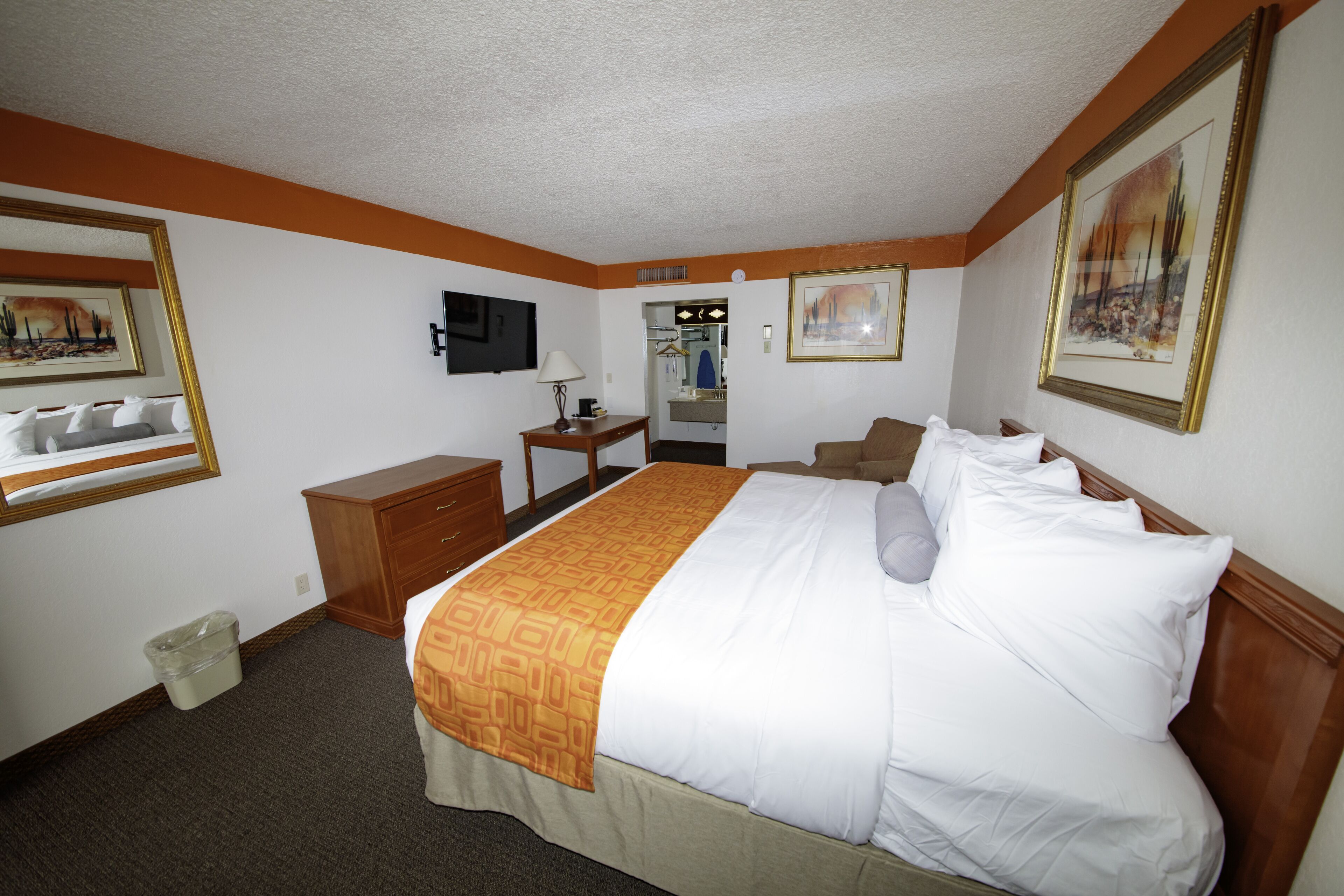 A hotel room with a bed, a desk, a chair, a TV, and a bathroom visible through an open door.