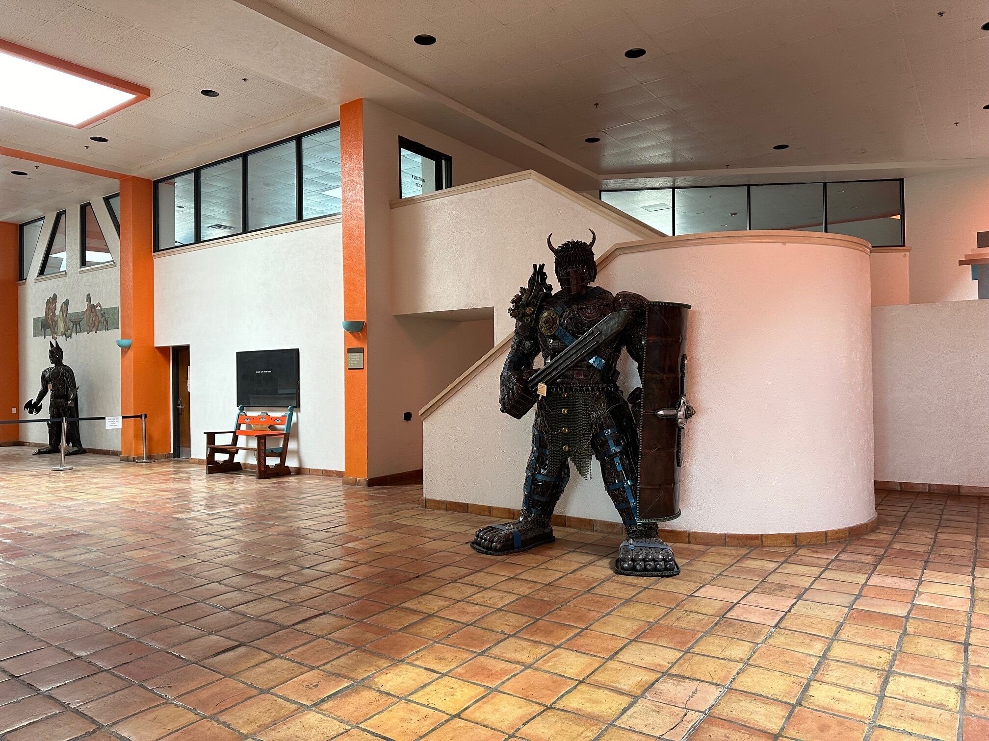 Un vestíbulo amplio con una gran estatua de un guerrero, una escalera y un mural en la pared.