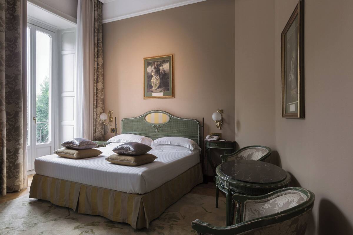 A bedroom with a large bed, a chair, a small table, and a painting on the wall.