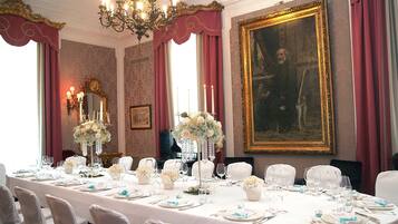 A formal dining room with a long table set for a meal, a chandelier, and a large framed painting on the wall.