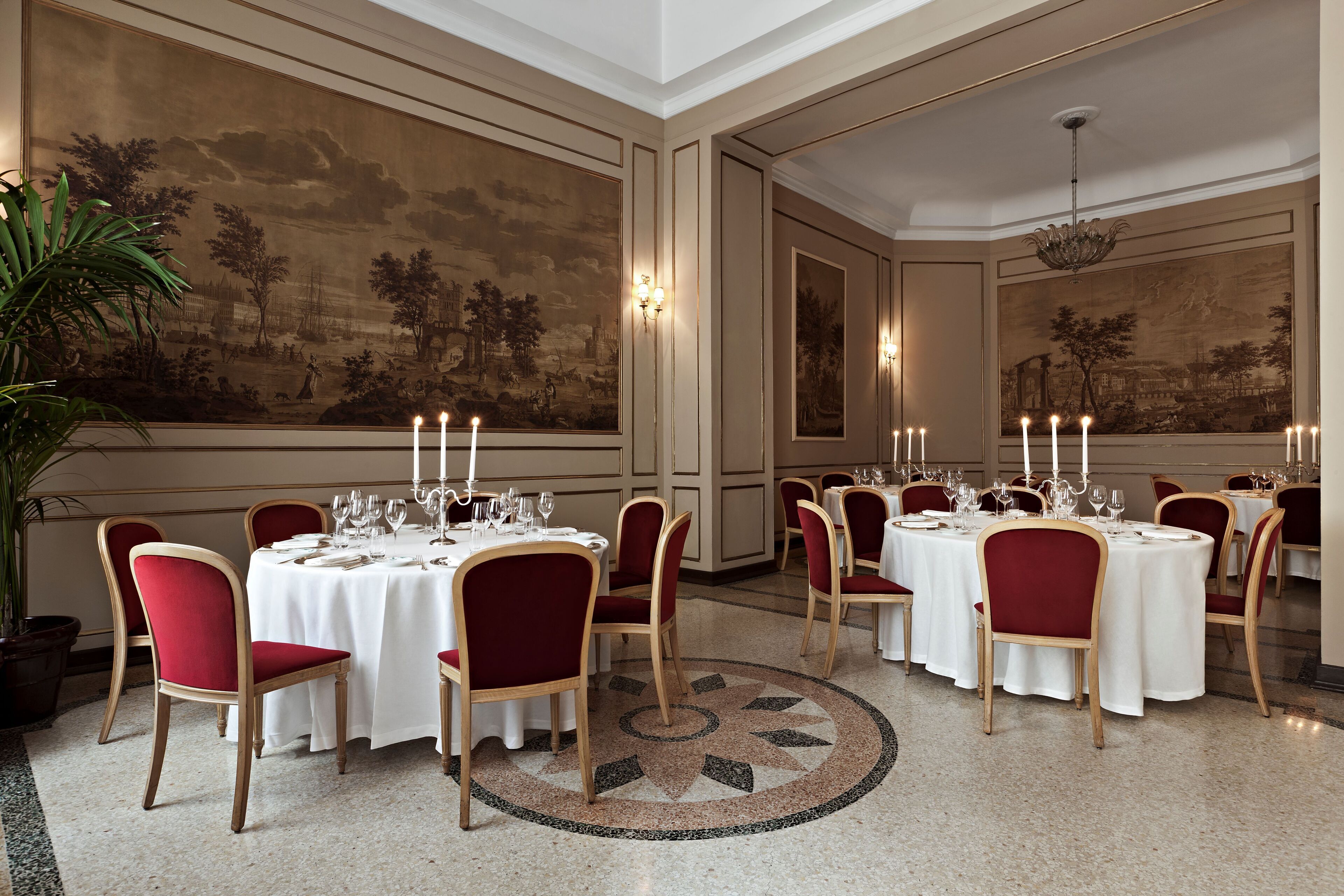A formal dining room with round tables, red upholstered chairs, and candle-lit centerpieces.