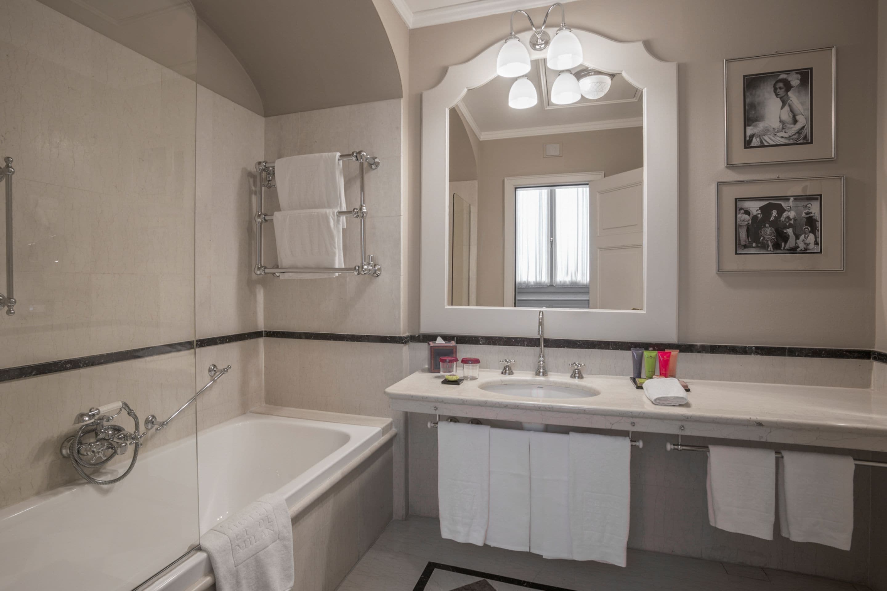 A modern bathroom with a bathtub, a sink, and a large mirror. There are towels hanging on the wall and a shower curtain rod.