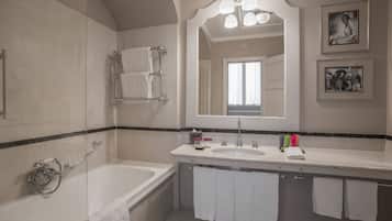 A modern bathroom with a bathtub, a sink, and a large mirror. There are towels hanging on the wall and a shower curtain rod.