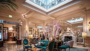 Un vaste hall d’entrée avec un plafond haut, des décorations somptueuses et un espace salon central agrémenté de canapés et de fauteuils verts moelleux.