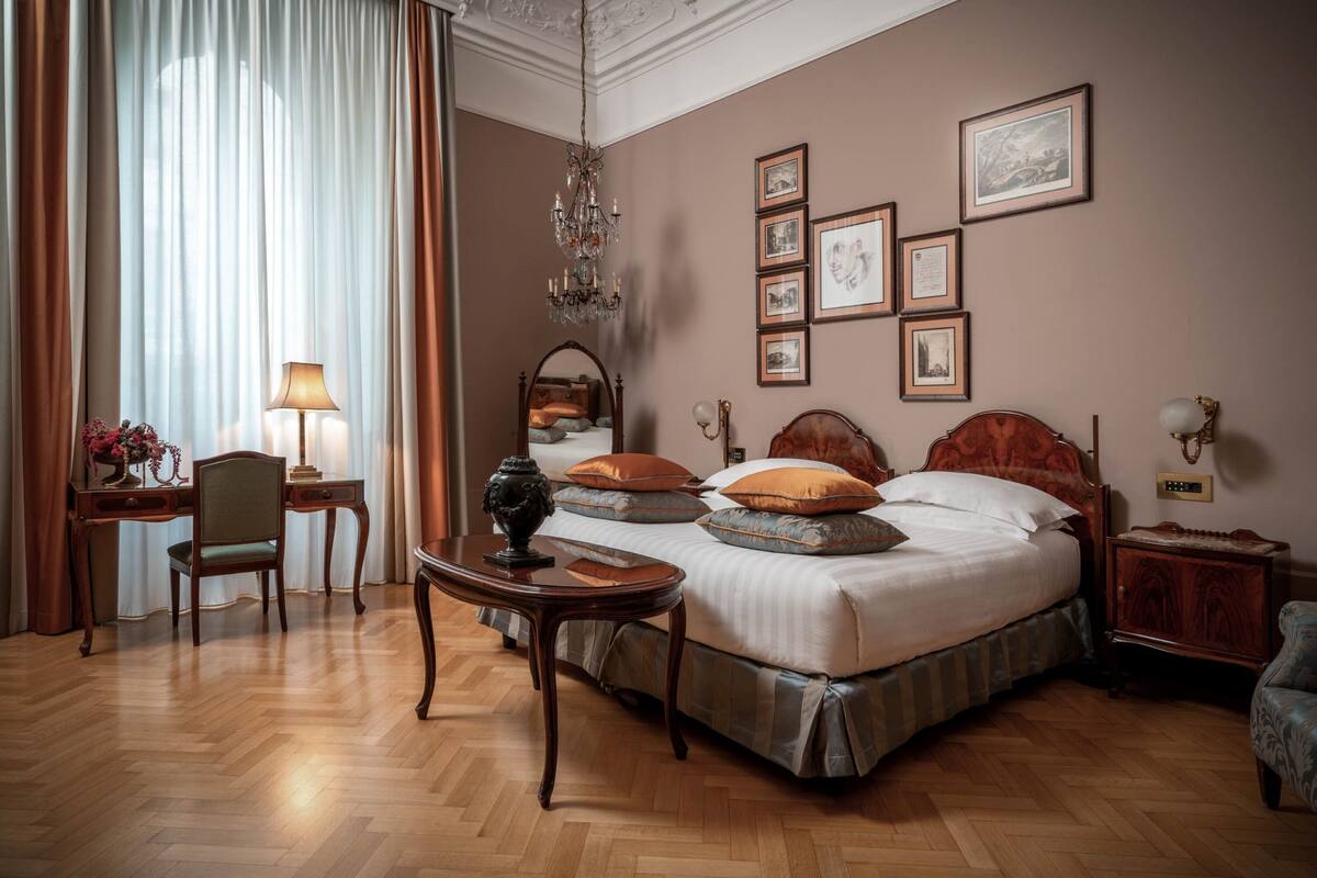 Une chambre d’hôtel avec un grand lit, un bureau, une chaise, une table de chevet et un lustre.