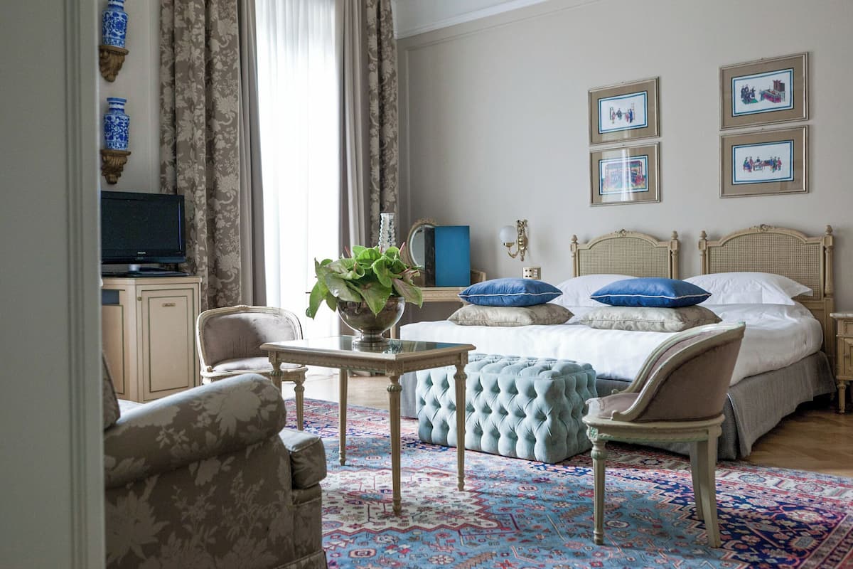 A bedroom with a bed, bedside tables, a TV, a chair, a table, and a large window.