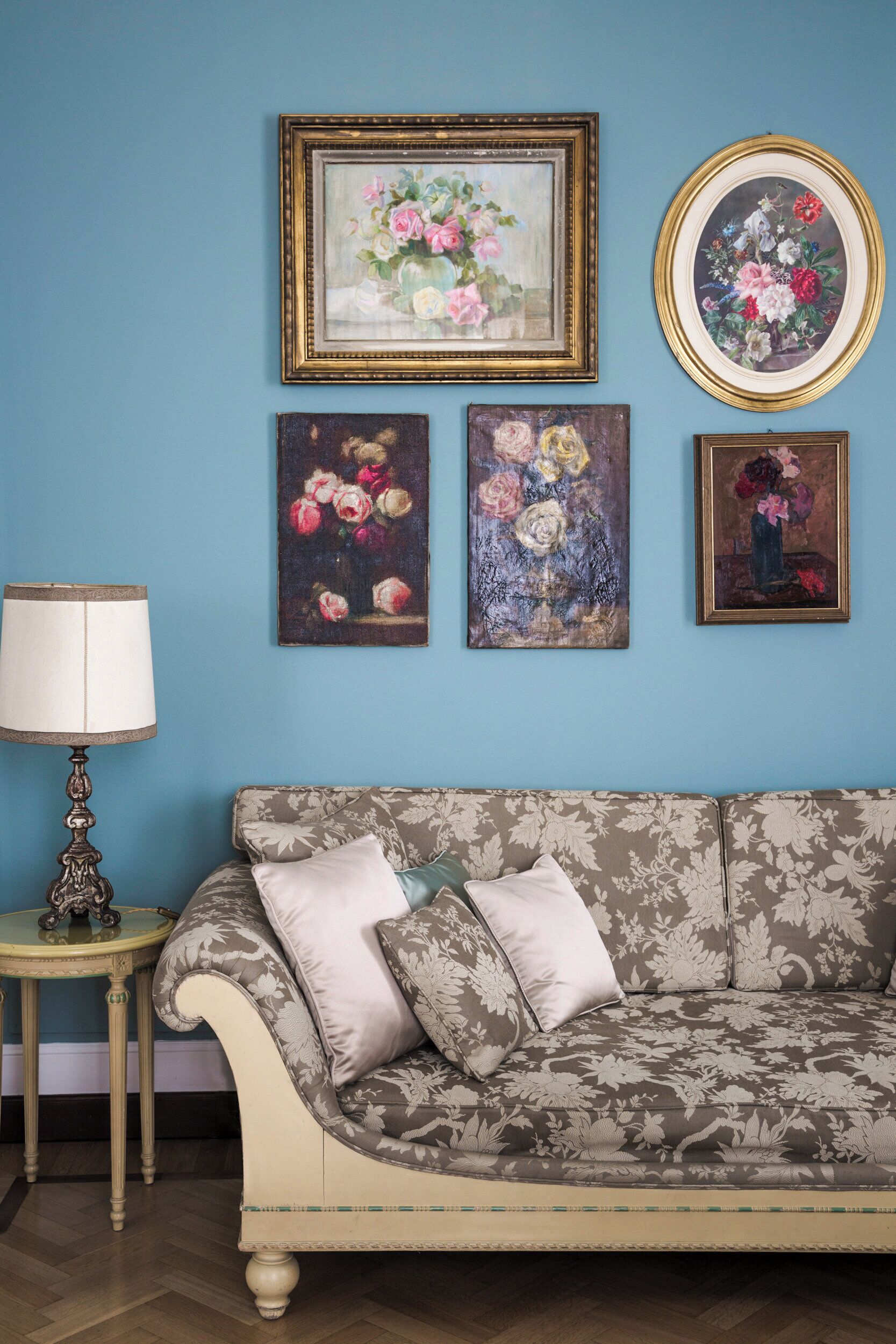 Una stanza con una parete blu, un divano a motivi floreali e tre quadri incorniciati con fiori.