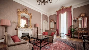 Une pièce dotée d’une cheminée, de deux fauteuils, d’une table basse et d’un grand miroir aux motifs dorés travaillés.