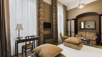 A hotel room with a bed, two armchairs, a sofa, a desk with a lamp, and a TV.