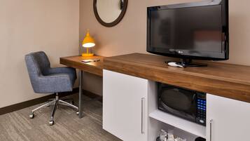 Ein Hotelzimmer mit Schreibtisch aus Holz, Fernseher, Mikrowelle, Stuhl und Lampe.