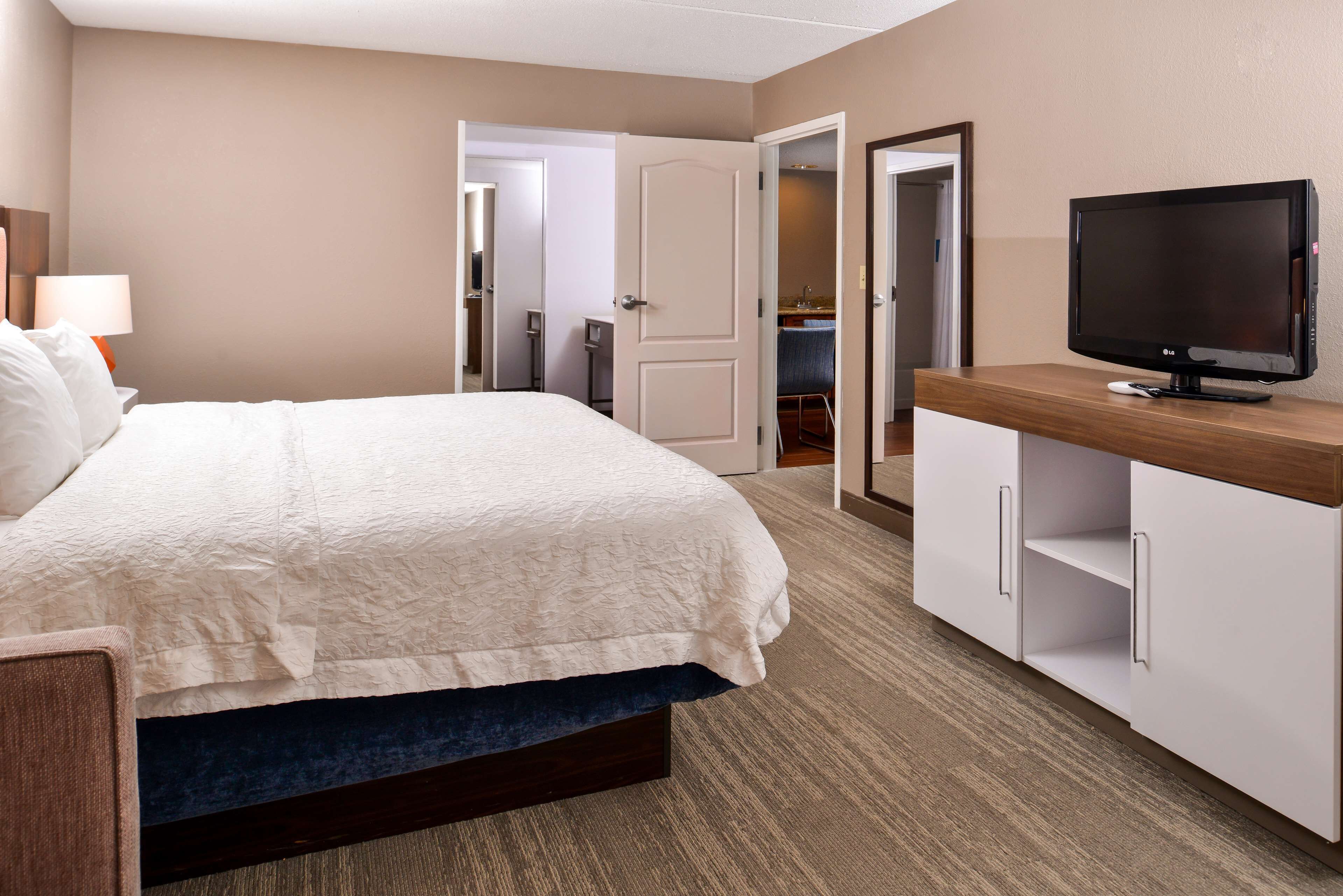 Una habitación de hotel con una cama, un televisor sobre un soporte de madera y un baño visible a través de una puerta abierta.