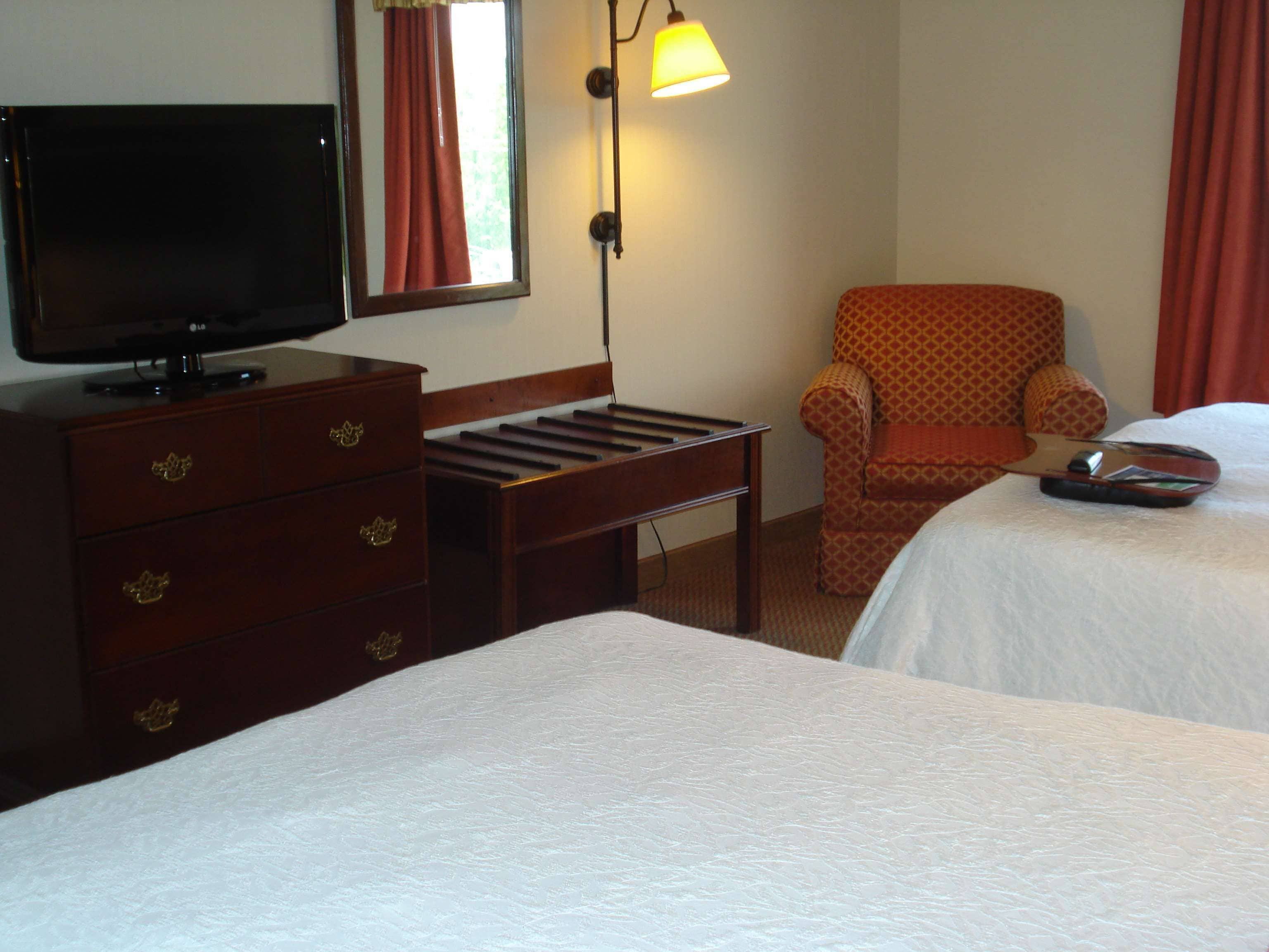 A hotel room with a TV on a dresser, a desk, two beds, and a chair.