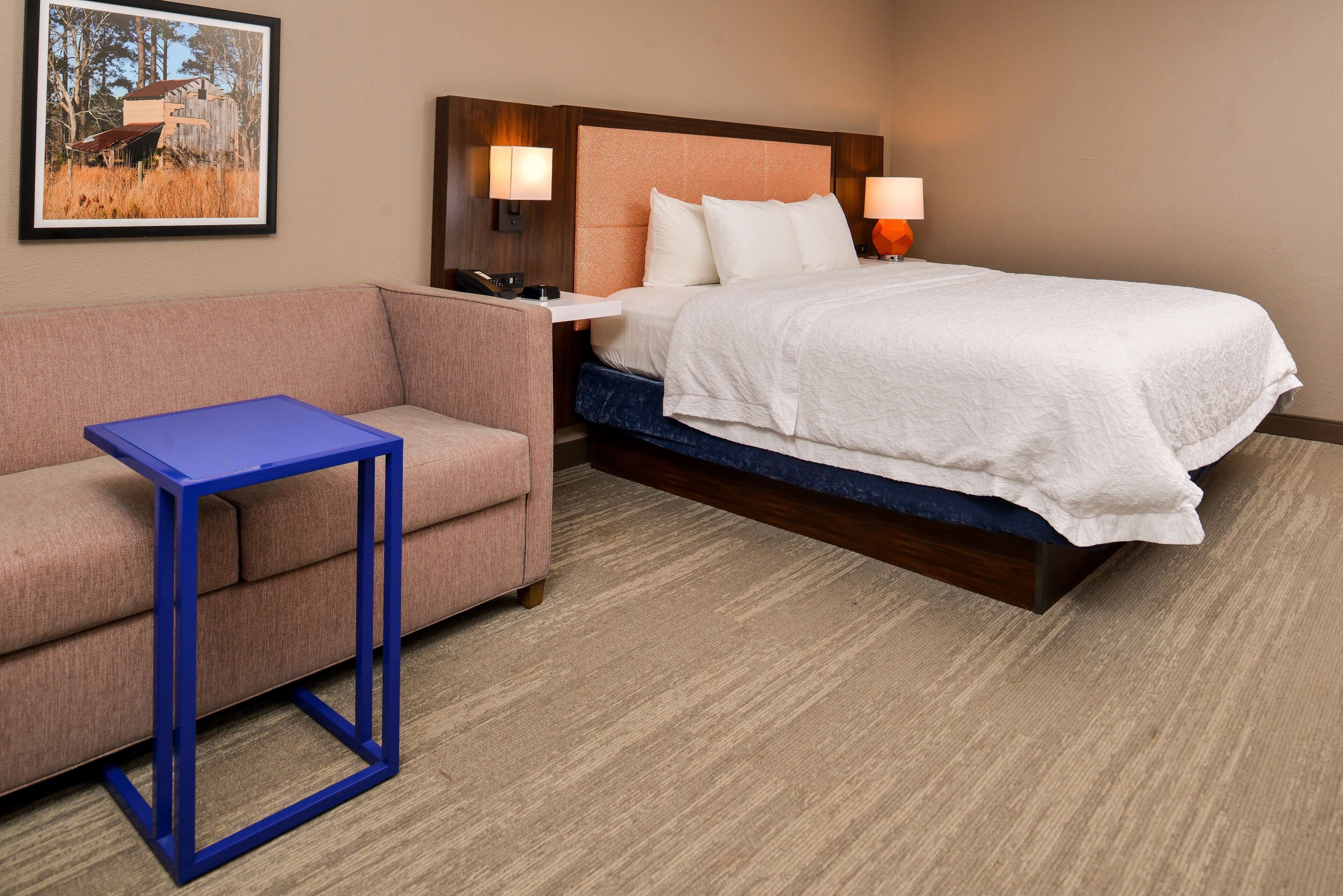 Une chambre d’hôtel avec un lit, une table de chevet bleue, un canapé et une lampe fixée au mur.