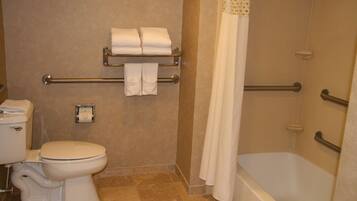Un baño con inodoro, toallero con toallas, dispensador de papel higiénico y bañera con cortina de ducha.