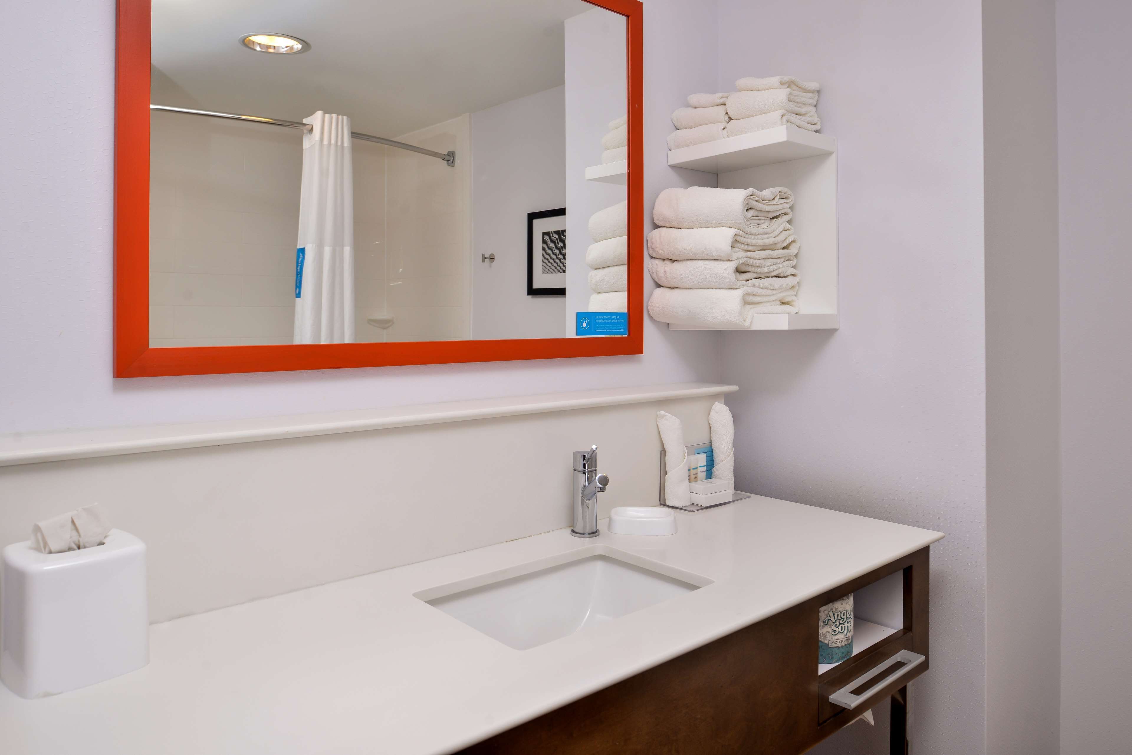 A bathroom with a white sink, a mirror with an orange frame, and a shelf with folded towels.