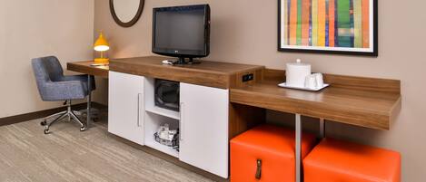 A hotel room with a desk, chair, TV, lamp, and storage cabinets.