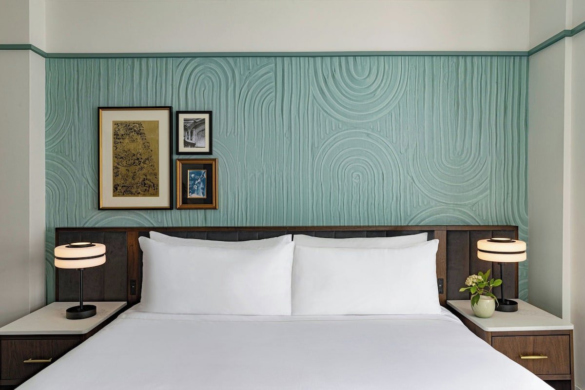 Une chambre d’hôtel avec un grand lit, deux tables de chevet avec des lampes et trois tableaux encadrés au mur.