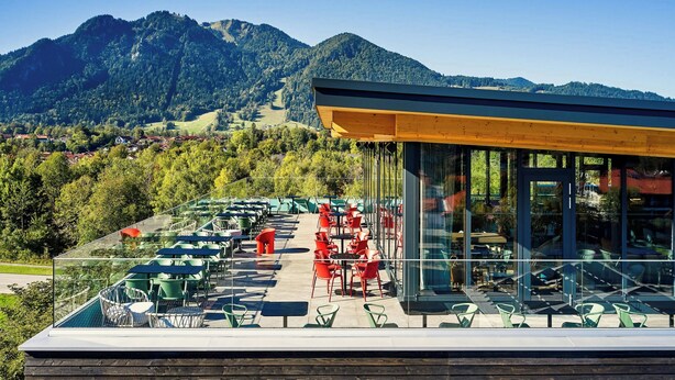 A terrace with outdoor seating, a glass enclosure, and a mountain view. - Flesslers Lenggries, a Tribute Portfolio Hotel (Lenggries)