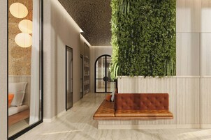 A modern lobby with a green vertical garden, a brown leather bench, and a glass wall with a seating area.