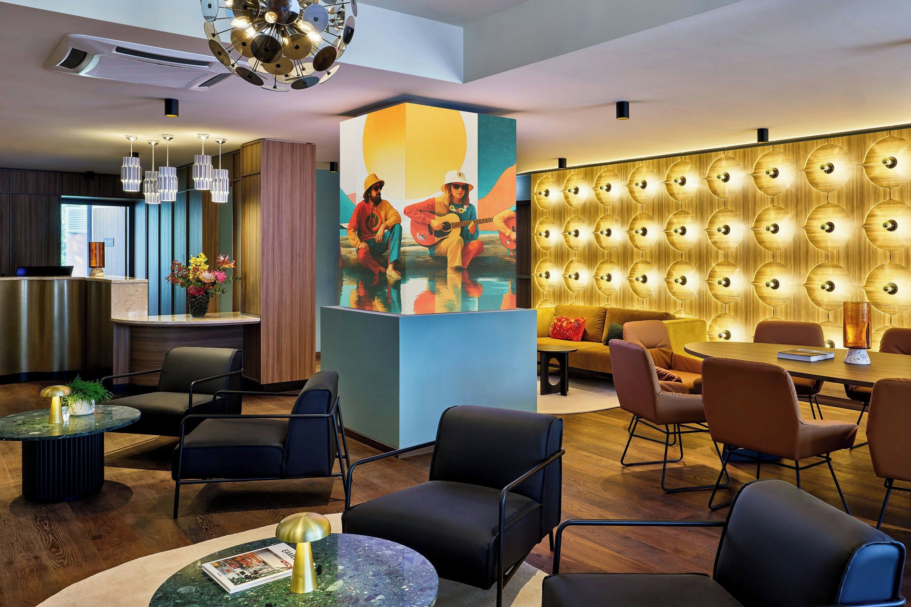 A modern hotel lobby with a reception desk, seating area, and a wall with a circular light fixture.