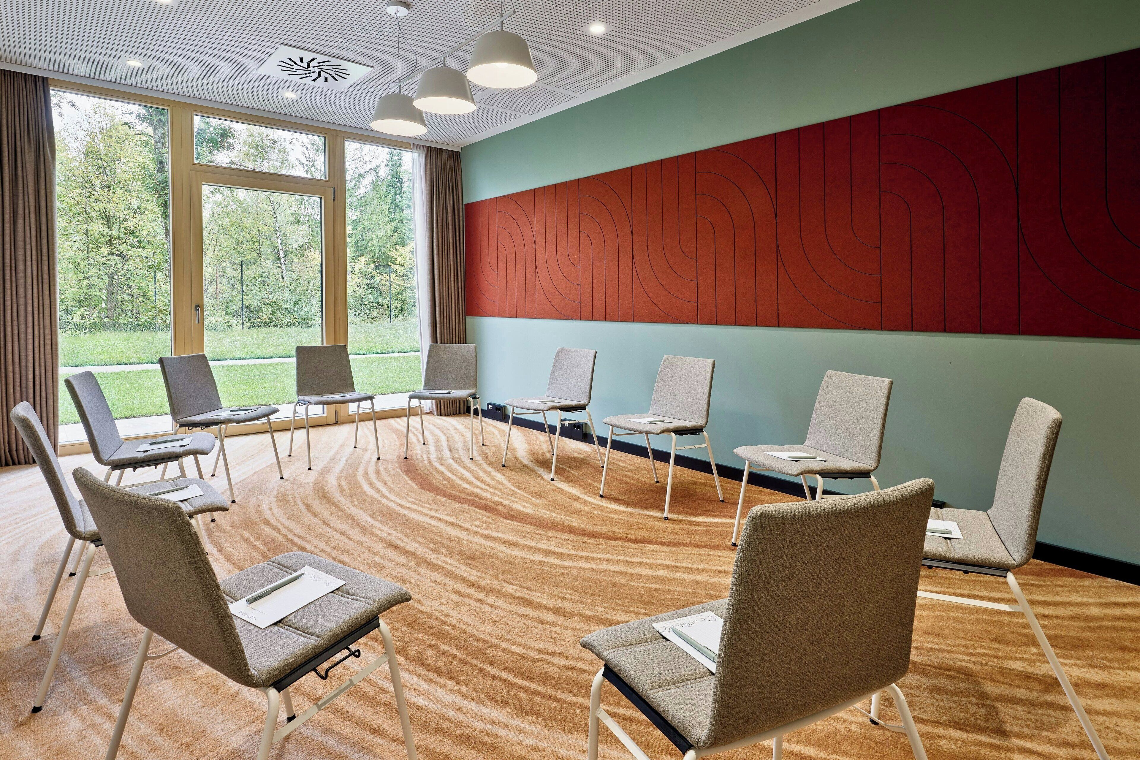 Une salle de conférence avec des sièges disposés en cercle, de grandes fenêtres et un plancher en bois.
