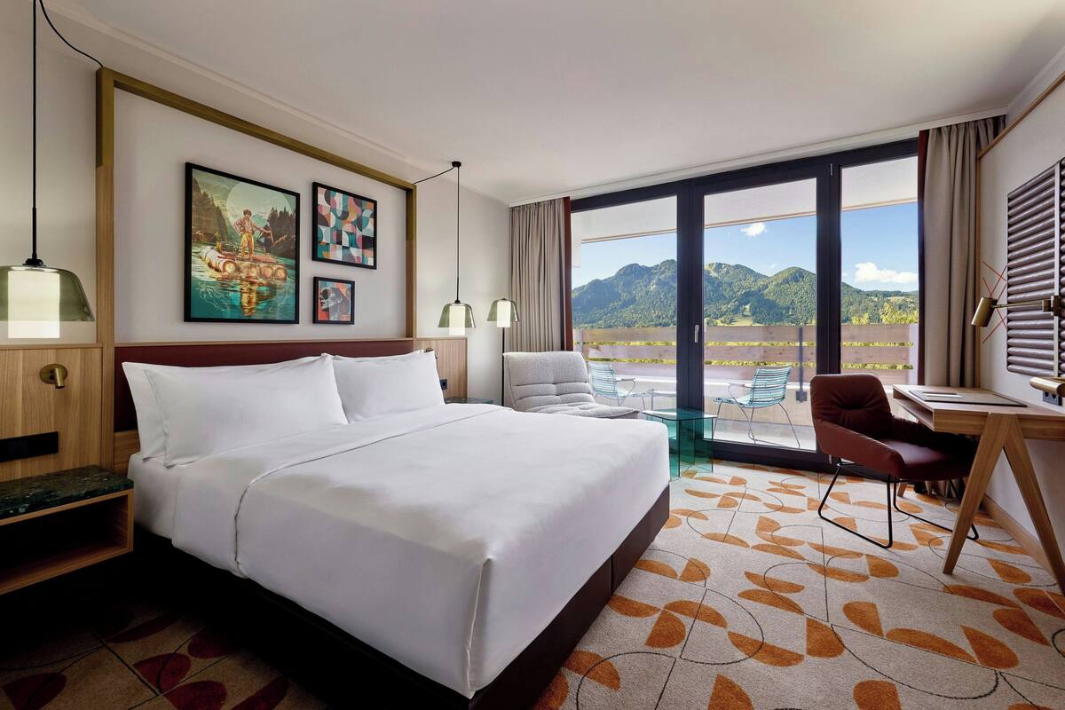 A hotel room with a large bed, a desk, and a view of mountains through the window.