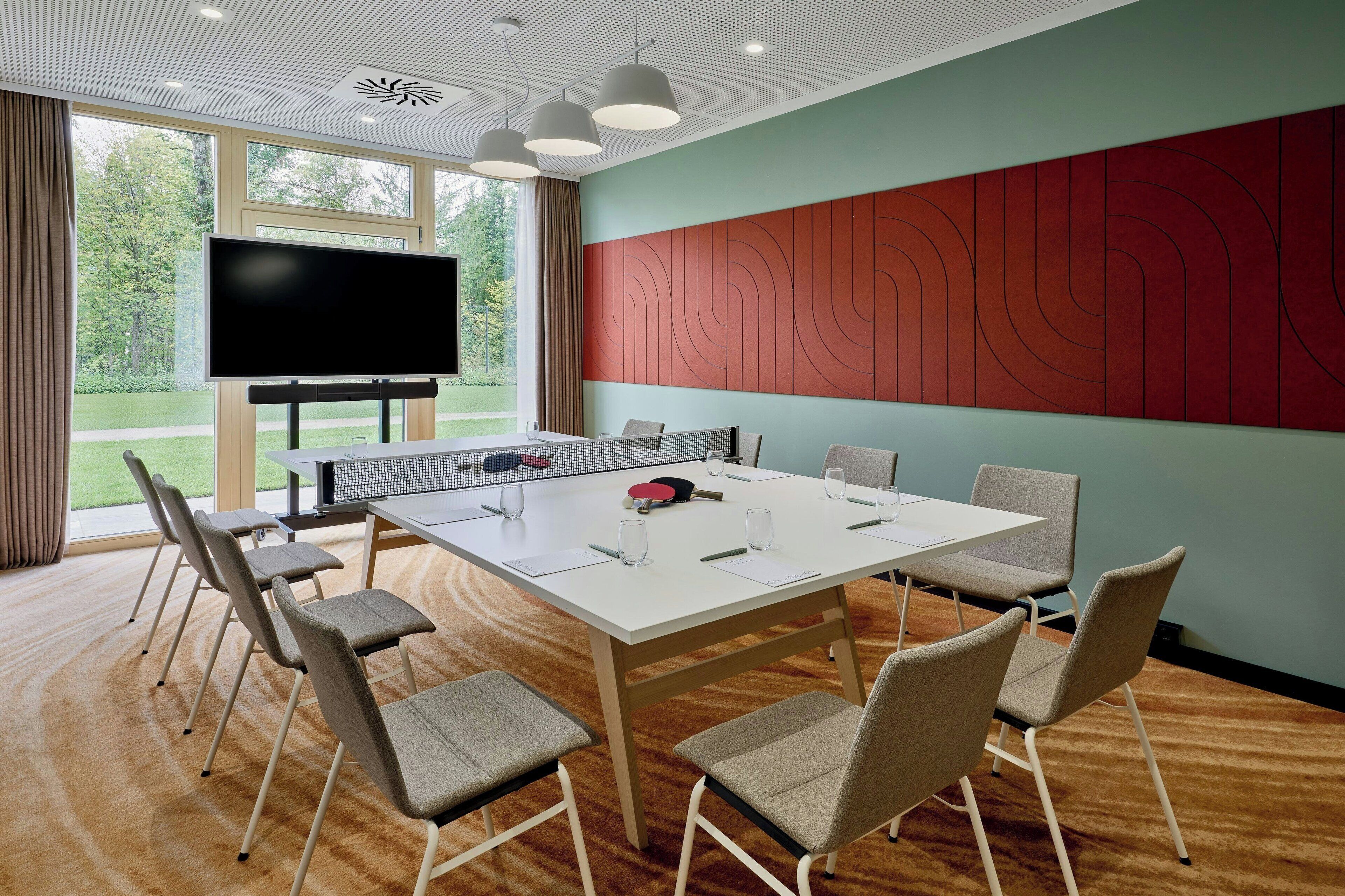 A conference room with a large table, chairs, a TV, and a view of the outdoors.